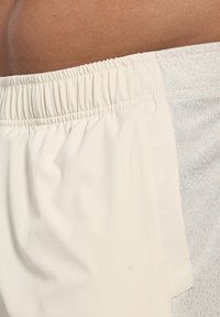 Ljust beige shorts har en elastisk midja och en mjuk, slät textur med en kontrasterande melerad panel på sidan.