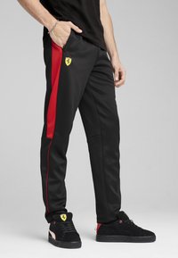 Schwarze Sporthosen mit einem roten Seitenstreifen und einem gelben Ferrari-Logo. Glattes Gewebe mit einer lockeren Passform und funktionalen Seitentaschen.