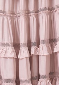 Tejido rosa claro con volantes en capas y un borde decorativo de encaje. Textura suave con un diseño fluido y un dobladillo estructurado.