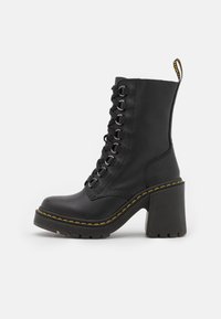 Stivaletto in pelle nera con tacco spesso, dotato di occhielli argentati e lacci neri, accentuato da cuciture gialle lungo la suola.