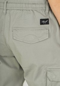 Helle graue Cargo-Hosen aus einem Baumwollmix, mit einem elastischen Taillenbund, seitlichen und hinteren Taschen sowie einem schwarzen Markenlabel auf der hinteren Tasche.
