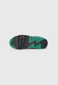 Sole tenisky Nike s čiernym a zeleným gumovým podpätkom. Obsahuje textúrovaný povrch s drážkami a vzormi pre trakciu. Zakrivený dizajn.
