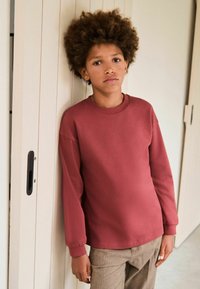 Bordoo pikkvarrukatega sviiter ümmarguse kaelusega, millele on sobitatud beežid mustrilised püksid. Kanga tekstuur näib olema pehme ja sile.