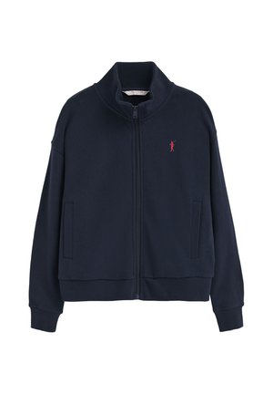 Chaqueta azul marino con cremallera, cuello alto, dos bolsillos delanteros, puños acanalados y pequeño logo rojo bordado en el pecho izquierdo.