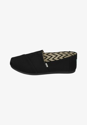 Black canvas slip-on shoes with a rounded toe and elastic panels. Textured black sole and patterned interior featuring chevron lines.