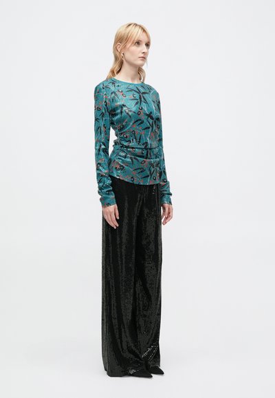 Haut à manches longues teal avec un motif floral ; associé à un pantalon noir à sequins taille haute et des chaussures noires à talons pointus.