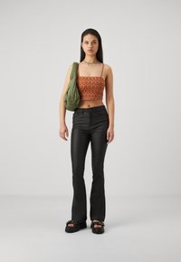 Pantaloni neri svasati, top corto a motivo arancione e borsa trapuntata verde. Le calzature presentano suole spesse con un dettaglio a tracolla.