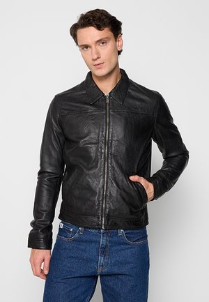 Czarna skórzana kurtka zapinana na zamek, z wyprofilowanym kołnierzem i bocznymi kieszeniami. Gładka tekstura i dopasowany krój, w połączeniu z niebieskimi dżinsami.