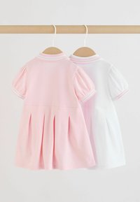 To korte plisserede kjoler med korte ærmer, den ene lyserød og den anden hvid, hængende på træbøjler på en lys træliste mod en hvid baggrund.