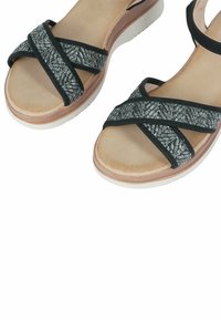 Sandali neri con cinturini intrecciati, caratterizzati da un accento in argento strutturato. Soletta beige chiaro e suola bianca con un dettaglio simile al legno.