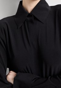 Black collared shirt with a buttoned front, featuring long, relaxed sleeves and a smooth, lightweight fabric texture.
