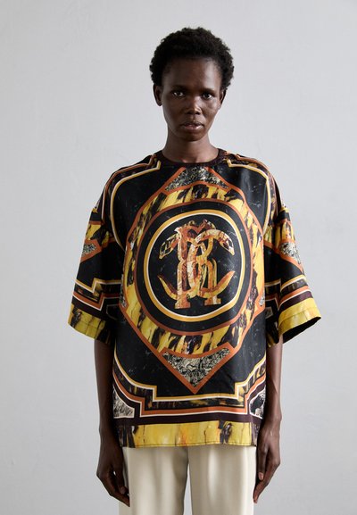 Chemise en satin oversize comportant un imprimé graphique audacieux en noir, or et orange, avec des manches larges et des détails d'ourlet contrastés.