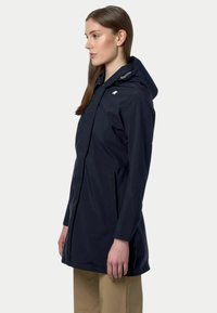 Parka imperméable noire avec capuche, dotée d'une fermeture éclair à l'avant, de poches latérales et d'un design minimaliste. Texture lisse et coupe mi-longue.