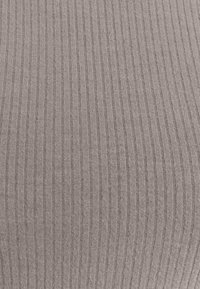 Gros plan d’un tissu tricoté côtelé marron clair avec des lignes verticales texturées et une apparence douce et extensible.