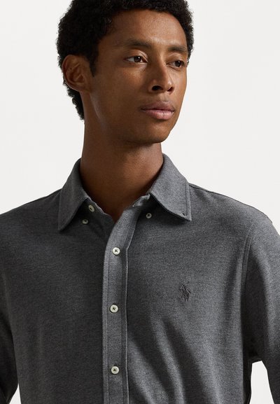 Šedá košile na knoflíky vyrobená z texturované látky, s límečkem, bílými knoflíky a malým logem na levé straně hrudi.