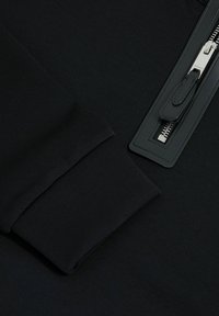 Hanorac negru cu un finisaj texturat, manșete riblate și un fermoar cu o curea din piele. Accentele din metal completează designul.