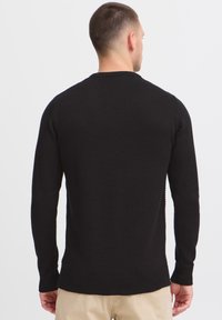 Zwarte gebreide trui met lange mouwen, ronde hals, geribbelde boorden en zoom, met een zachte textuur en een getailleerd silhouet.