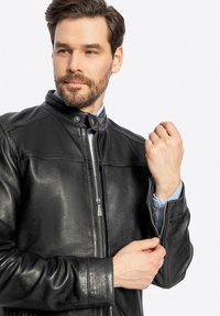 Giubbotto in pelle nera con colletto alto, chiusura frontale a zip e polsini con zip. Texture liscia, cuciture minime e vestibilità sartoriale.