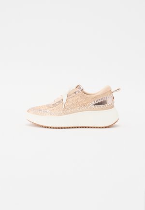 Sneaker con tomaia intrecciata in un beige chiaro e dettagli metallici, suola spessa bianca e design con lacci e cuciture decorative.