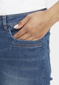 Vidēji zilas džinsa bikses ar klasisku piegriezumu, ar priekšējo kabatu un kontrastējošu šuvju detaļām. Audums izskatās mīksts ar vieglu spīdumu.