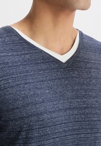 Marinblå v-ringad t-shirt med en texturerad mönster, med en kontrasterande vit detalj på insidan av kragen. Tyget verkar mjukt och lätt.