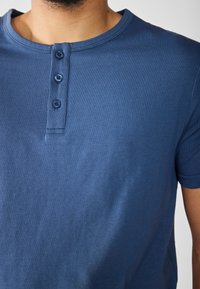 T-shirt a maniche corte in cotone di colore blu, con scollatura rotonda e patta con tre bottoni nella parte anteriore, caratterizzato da una texture liscia.