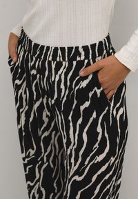 Black and white striped pants with a crinkled texture, elastic waistband, and side pockets. Stripes have a wavy pattern.