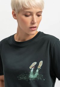 Zwarte katoenen t-shirt met een grafisch ontwerp van voeten in sneakers ondergedompeld in groene water, met een ronde hals en korte mouwen.