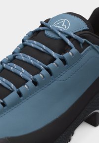 Modrá a černá turistická bota La Sportiva s modrými šňůrkami se vzorem protaženými širokými očky.