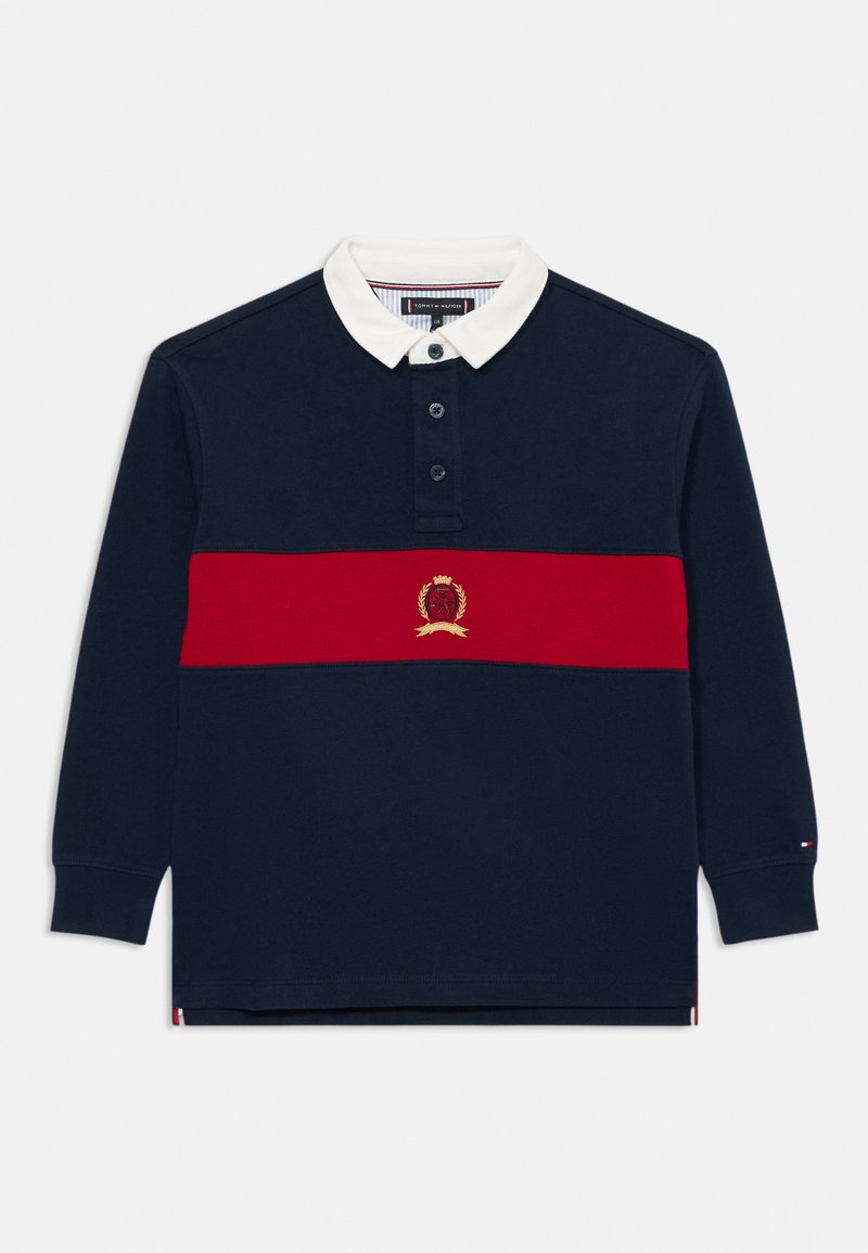 Polo de manga larga en color navy con cuello blanco, franja horizontal roja y emblema bordado. Cuenta con una tapeta de tres botones y puños acanalados.