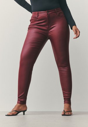 Burgundy fitted pants made of a shiny, stretch material with a high waist. Features five pockets and button closure. Paired with black heels.