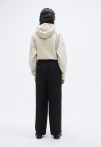 Μπεζ κοντή μπλούζα με κουκούλα, συνδυασμένη με μαύρο παντελόνι φαρδύ κανονικής μέσης. Το υλικό φαίνεται μαλακό με χαλαρή εφαρμογή.
