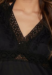 Blusa negra con escote en V, adornada con encaje y patrones florales bordados en el escote y la cintura. Textura de tela suave.