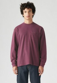 Camiseta de manga larga color burdeos hecha de algodón, con cuello redondo y un bolsillo en el pecho. Textura suave con un corte relajado y dobladillo recto.