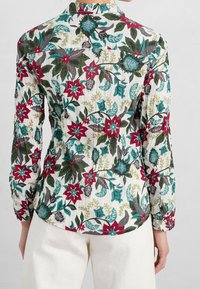 Blusa floreale in tessuto leggero con una base bianca e stampati botanici colorati in rosso, teal e verde, maniche lunghe e colletto con bottoni.