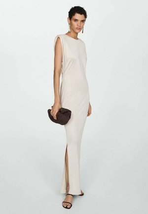 Beige Maxikleid mit gerader Silhouette, kurzen Ärmeln, seitlichen Schlitzen und glatter Textur. Kombiniert mit einer dunklen gewebten Clutch und schwarzen Sandalen.