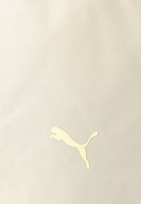 Επιφάνεια από μπεζ ύφασμα με μια μικρή, ανοιχτό κίτρινη σιλουέτα ενός πηδώντας πούμα στο κέντρο.