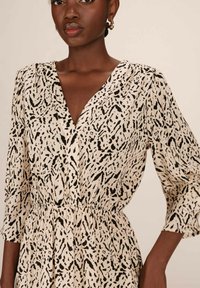 Robe à motifs lavande et noir en tissu léger, avec un décolleté en V, des manches trois-quarts et une taille élastiquée.