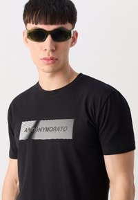 Black T-shirt featuring a white graphic design with diagonal lines and text, paired with fitted green sunglasses.