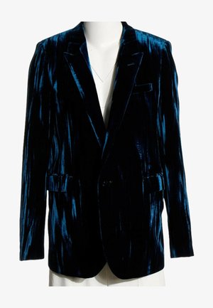 Blazer de terciopelo azul oscuro con una textura brillante, mostrado sobre un torso de maniquí blanco, con solapas con muescas y bolsillos con solapa.