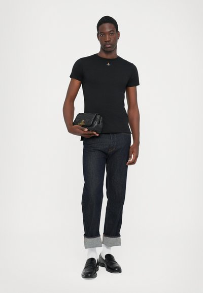 Sort kortærmet t-shirt med et lille emblem, kombineret med mørk denim jeans og sorte loafers. Inkluderer en struktureret sort clutchtaske.