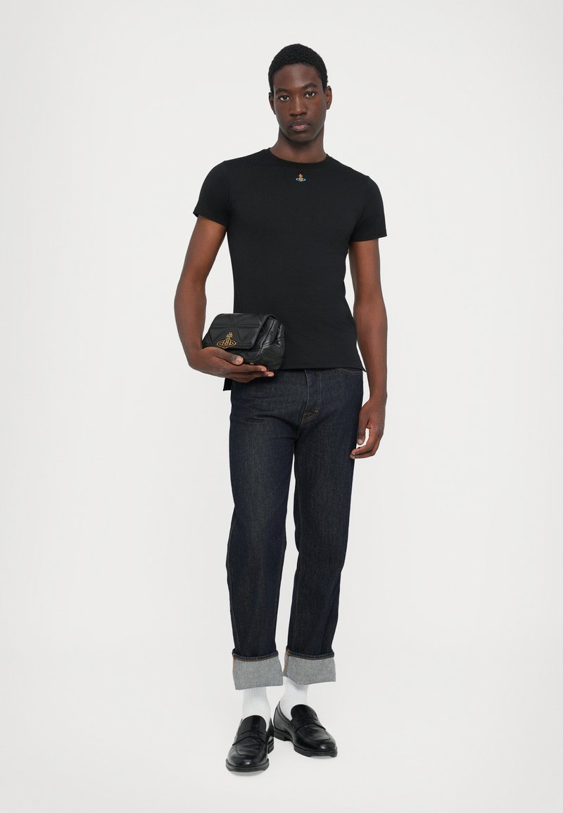 Un tricou negru cu mânecă scurtă cu un mic emblem, combinat cu blugi dark denim și loafers negri. Include o geantă de tip clutch texturată neagră.