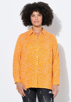 Camisa naranja de manga larga con un patrón de estampado de leopardo, con dobladillo recto. Llevada con jeans negros desgastados.