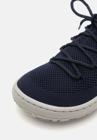 Baskets en maille navy avec des lacets gris et un empiècement texturé. Elles possèdent une semelle en caoutchouc gris clair avec un motif pour une bonne traction.