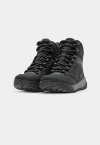 Botas de caminhada pretas com parte superior impermeável, sola com aderência texturizada, ilhós reforçados e atacadores duradouros. Design de média altura para suporte.