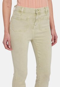 Lichtgele denim jeans met een hoge taille, twee achterzakken en een gladde textuur. Voorzien van een sluiting met een voorknop en riemlussen.