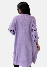 Cárdigan de punto morado de corte holgado, con una textura en la tela y acentos de estrellas negras en las mangas. Larga longitud con ribete acanalado en el dobladillo y los puños.