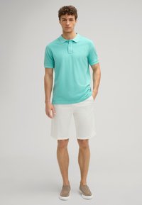 Turquoise katoenen polo shirt met een kraag en korte mouwen, gecombineerd met witte shorts en bruine instap schoenen. Eenvoudig en casual ontwerp.