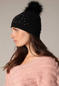 Zwarte gebreide beanie met een fluffy pompon bovenop, versierd met verspreide metalen studs, met een snug fit en een zachte textuur.