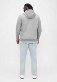 Šedá kapucňová mikina s jemnou textúrou, priliehavý strih a rebrované náplety, skombinovaná s svetlomodrými džínsami a bielymi teniskami.